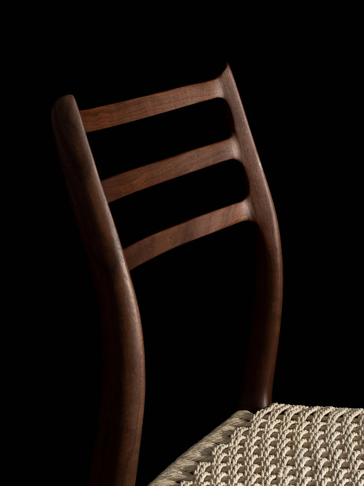 Close-up detail of the ergonomically curved ladder backrest on The Haven Dining Chair, crafted from premium solid Black Walnut wood.