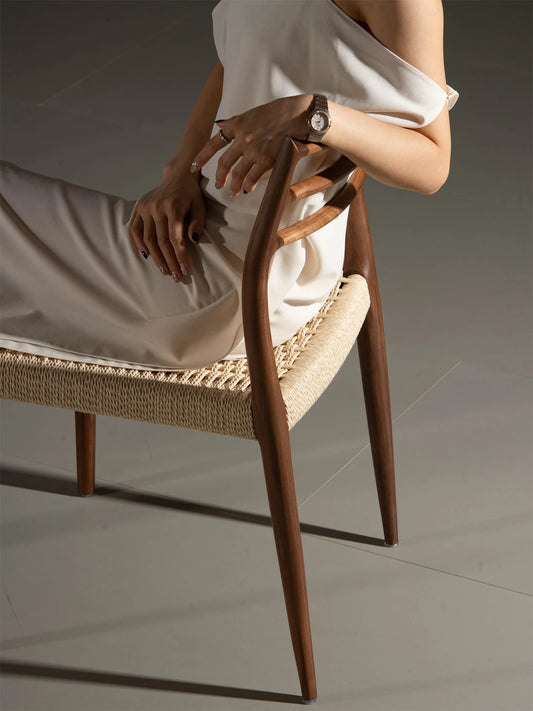 Lifestyle shot of a woman relaxing in The Haven Dining Chair, highlighting the comfortable woven seat and the supportive solid Black Walnut backrest.