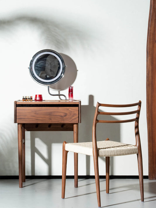 The Haven Dining Chair used as an elegant seating option at a solid Black Walnut makeup vanity desk in a bright, modern room setting.