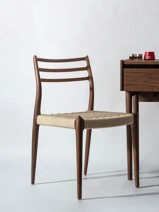 The Haven Dining Chair featuring a woven seat and solid North American Black Walnut frame, placed elegantly next to a modern vanity desk.