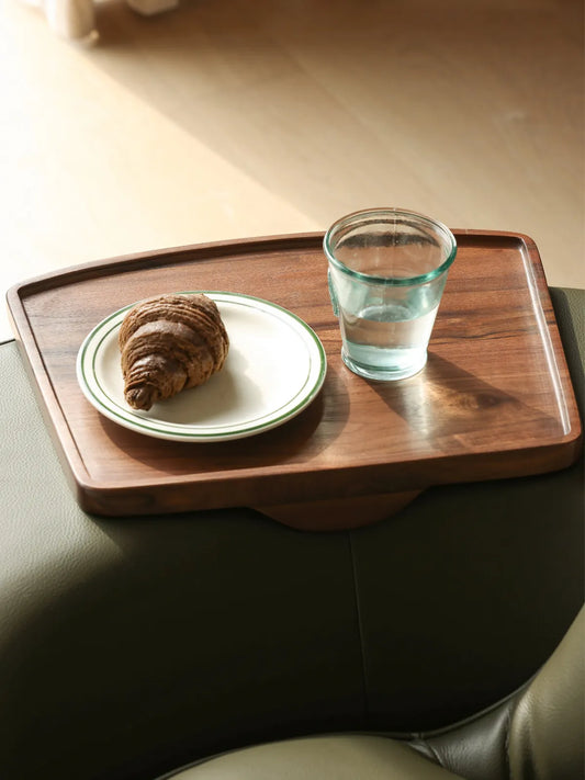 Close-up detail of the solid North American Black Walnut side tray attached to The Helios Retreat Swivel Recliner, holding a small plate and glass of water.