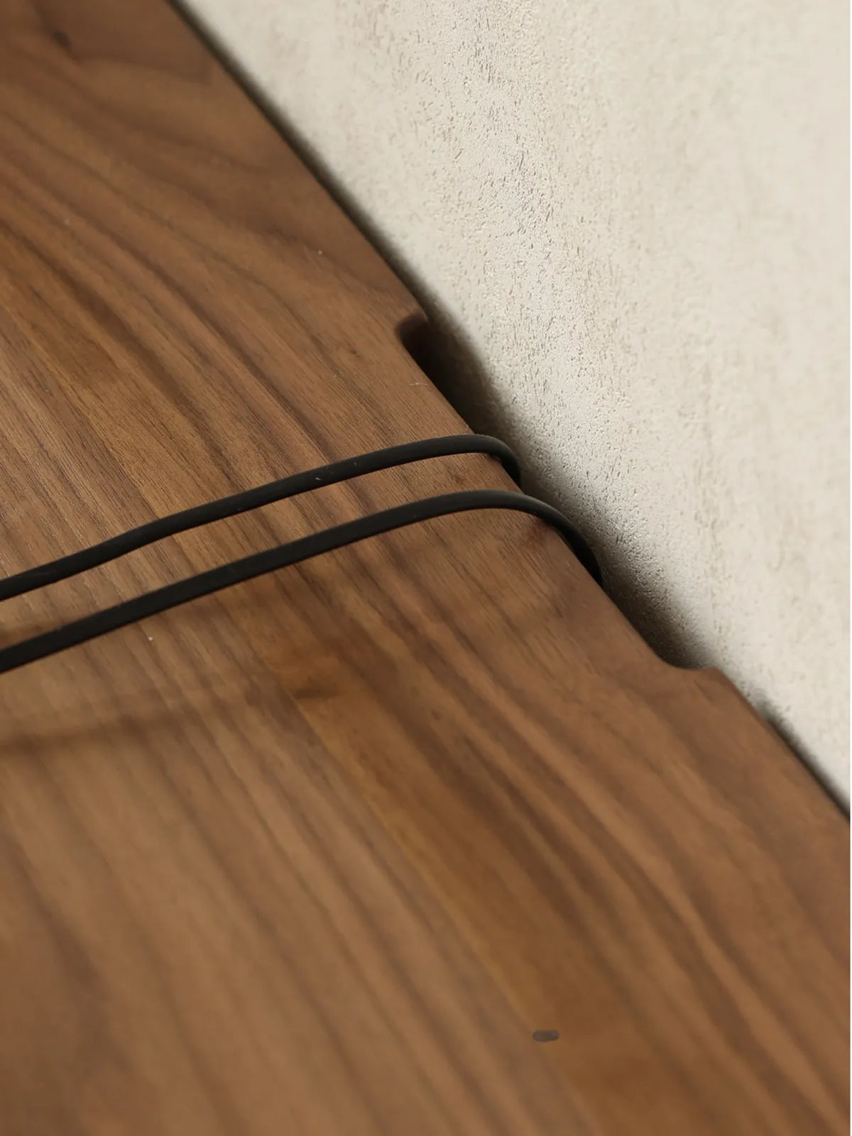 Close-up of the back edge of The Pebble Media Console against a wall, showing a convenient cable management cutout with cords passing through seamlessly.