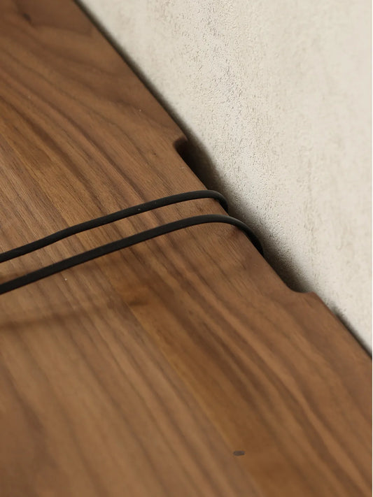 Close-up of the back edge of The Pebble Media Console against a wall, showing a convenient cable management cutout with cords passing through seamlessly.