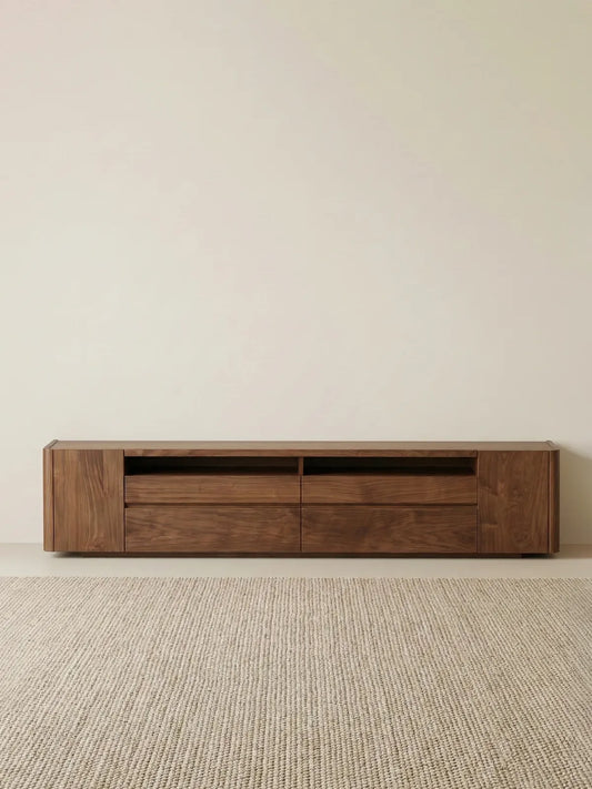 Straight-on minimalist shot of The Pebble Media Console in walnut, placed on a textured rug against a blank beige wall.