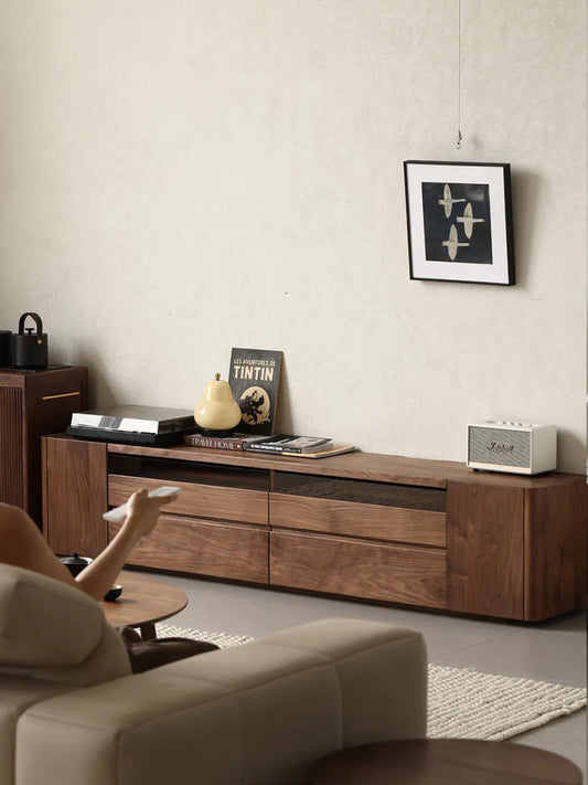 A person sitting on a sofa using a remote control, with The Pebble Media Console styled in a warm, modern living room setting.