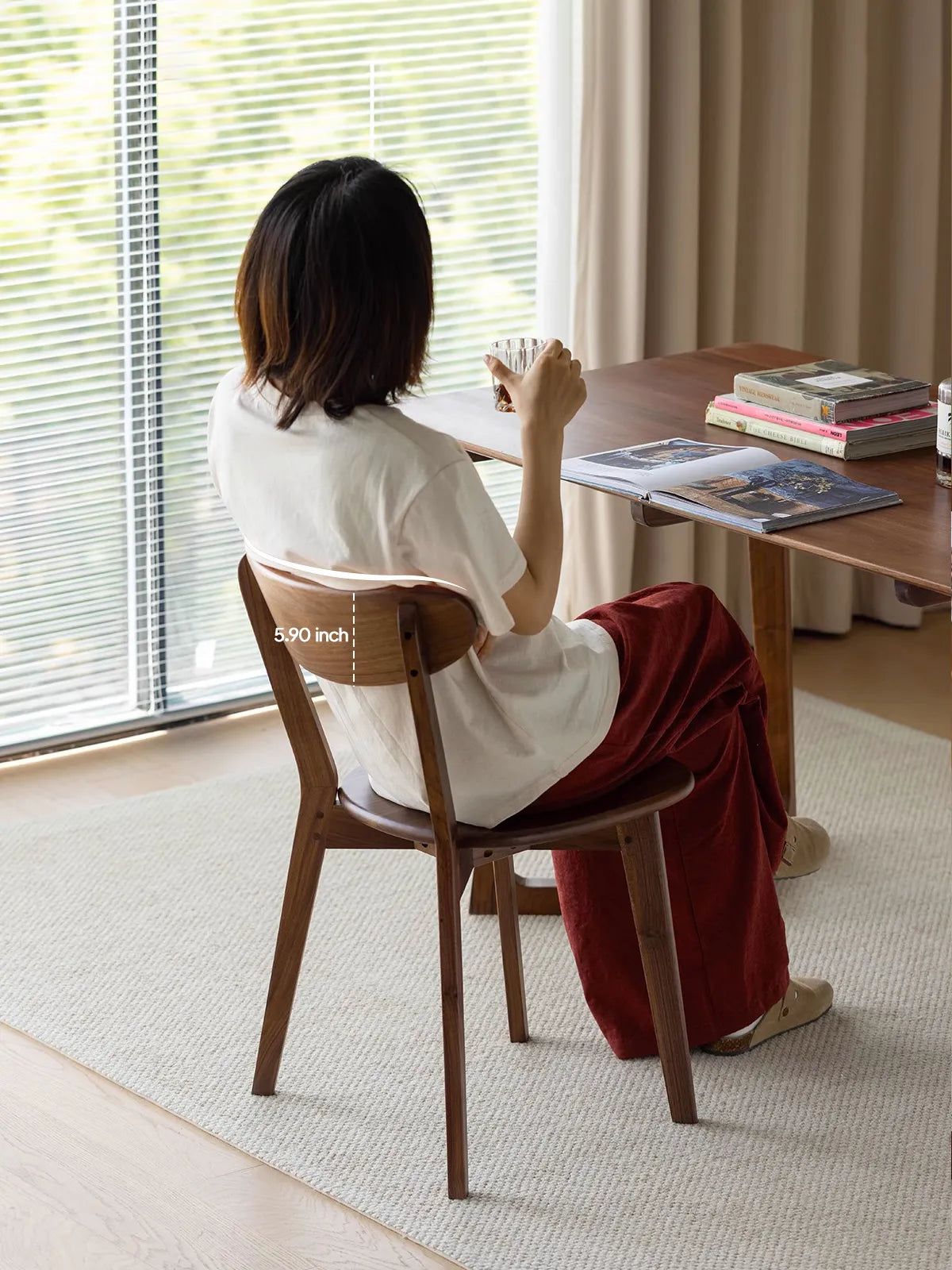 A woman sitting comfortably in The Sylva Dining Chair, demonstrating the ergonomic 5.90-inch curved backrest crafted from solid North American Black Walnut.