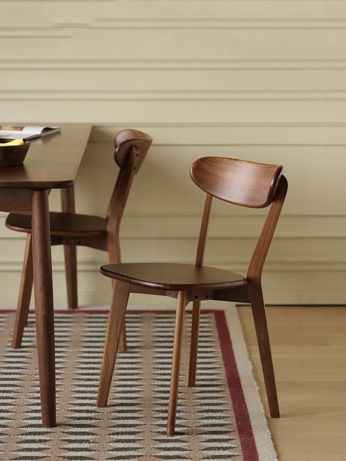 Side profile of The Sylva Dining Chair, emphasizing the minimalist angled legs and elegantly curved solid Black Walnut backrest.