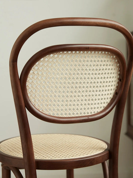 Close-up of the oval handwoven rattan cane backrest and curved walnut frame on the Tovin dining chair