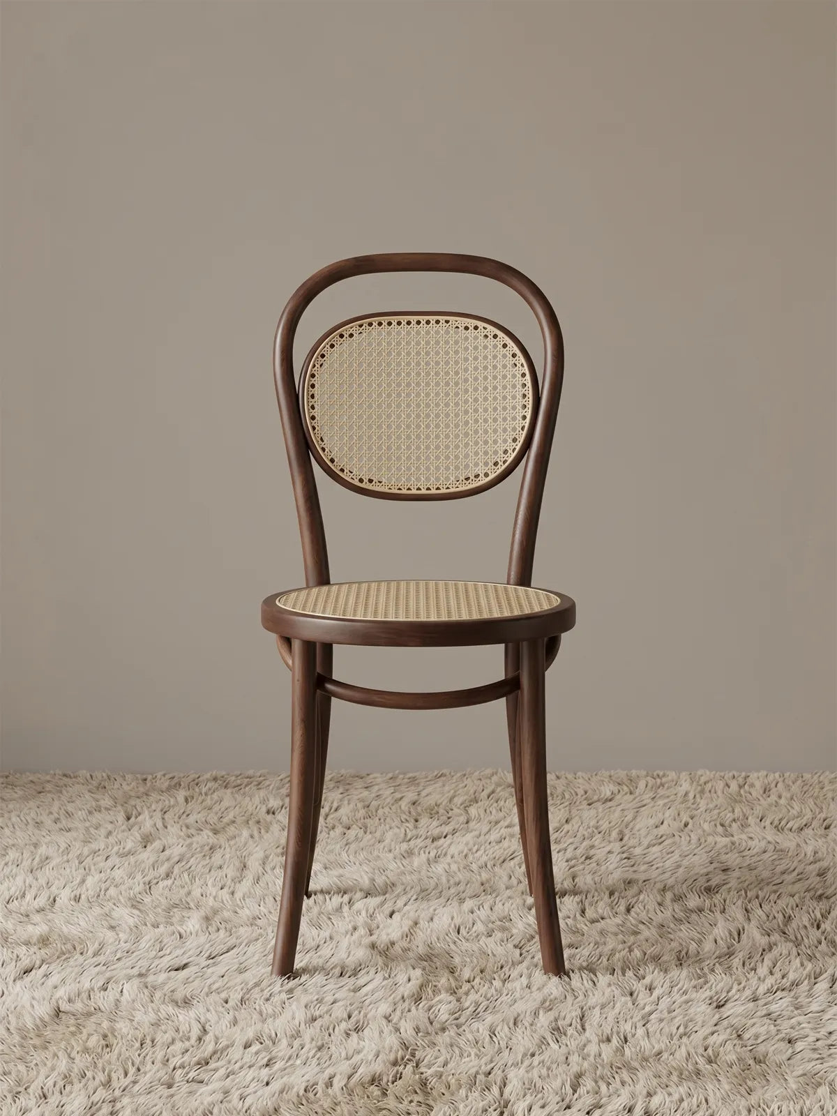 Tovin bentwood dining chair in solid walnut with handwoven cane seat and oval cane backrest, front view on textured rug
