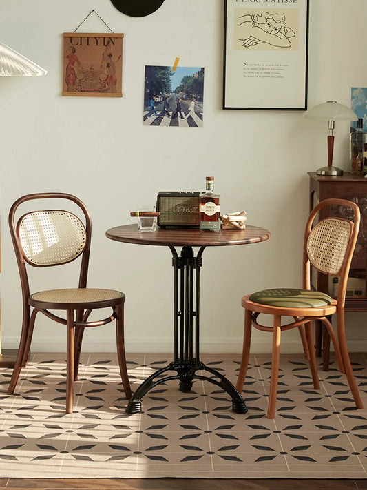 Two Tovin bentwood cane dining chairs flanking a round walnut bistro table in a styled café-inspired room