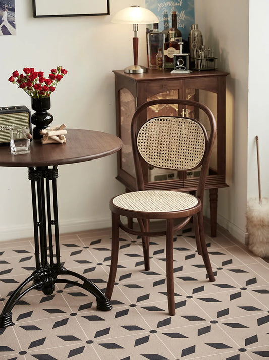 Tovin walnut bentwood cane dining chair viewed from behind beside a round table and walnut display cabinet