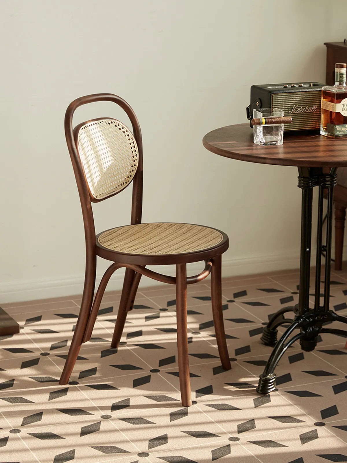 Tovin walnut bentwood cane dining chair seen from a three-quarter angle beside a round bistro table on patterned tile floor