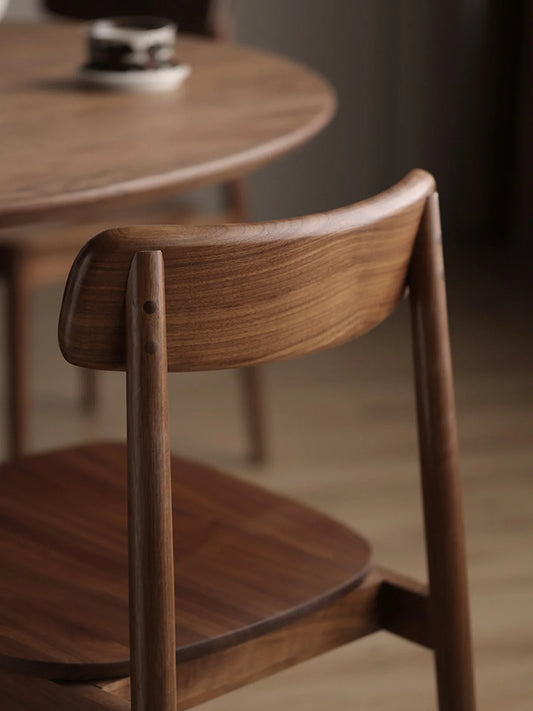 Close-up of a solid American black walnut dining chair showing the sculpted low backrest, rich grain, and rear post joinery detail.
