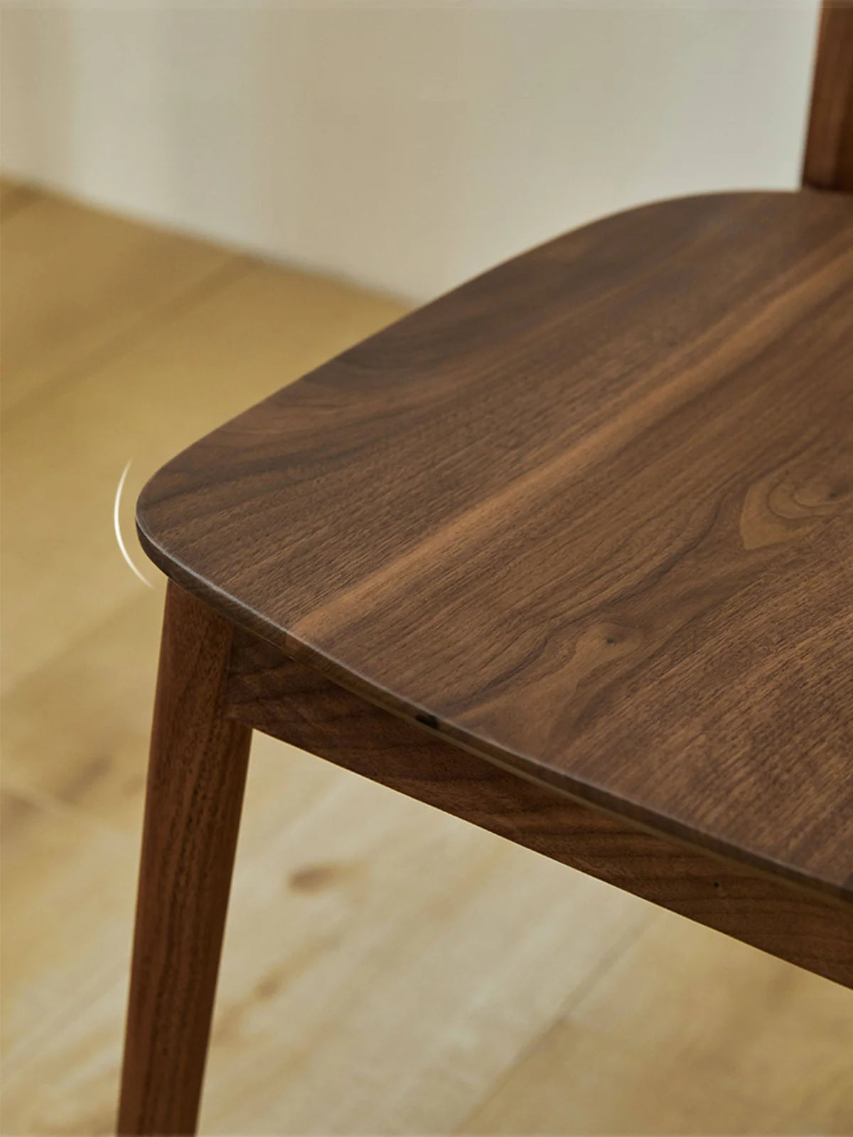 Close-up of the walnut dining chair seat corner showing the softened edge profile, seat thickness, and front leg transition.