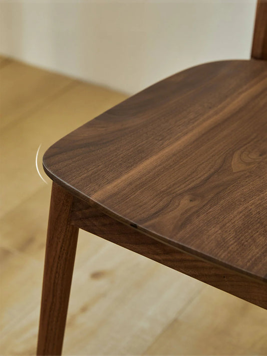 Close-up of the walnut dining chair seat corner showing the softened edge profile, seat thickness, and front leg transition.