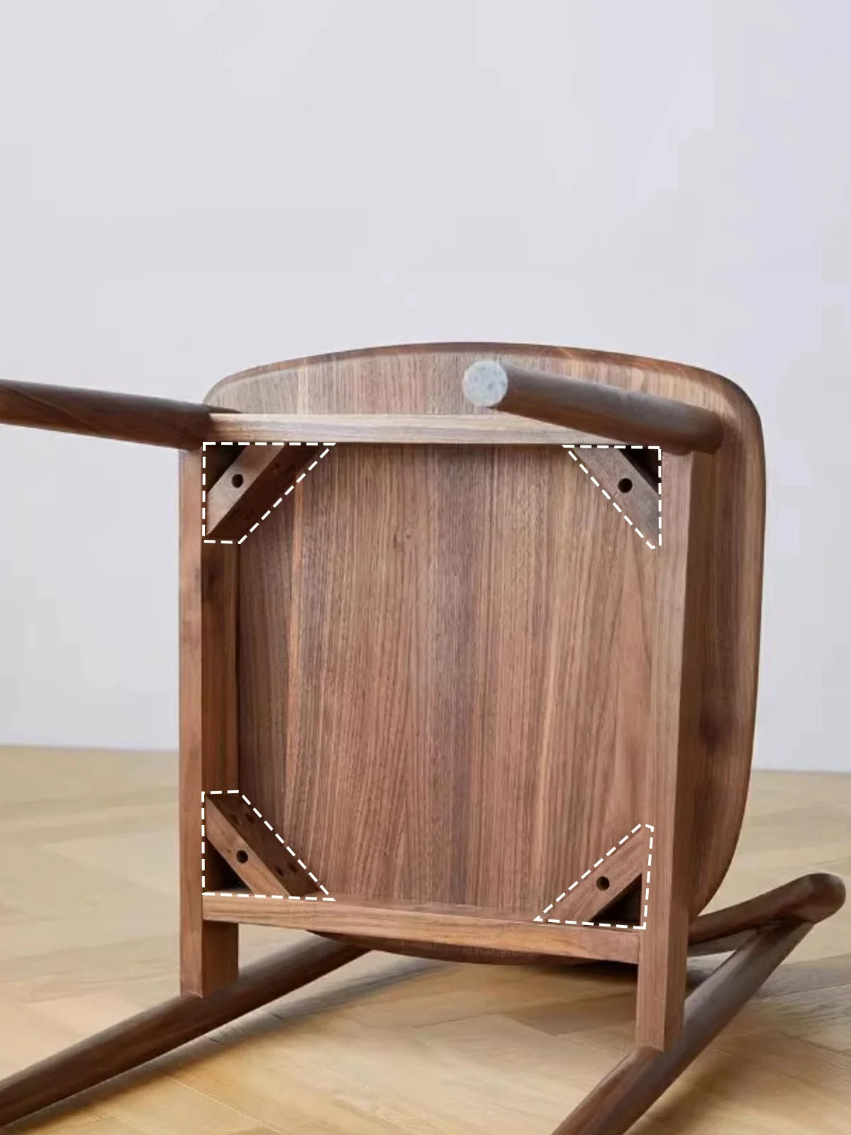 Underside view of a walnut dining chair showing the solid wood seat panel, apron frame, and reinforced corner bracing construction.