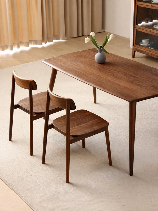 Two walnut dining chairs placed around a rectangular solid wood dining table, viewed from above to show layout, scale, and design cohesion.