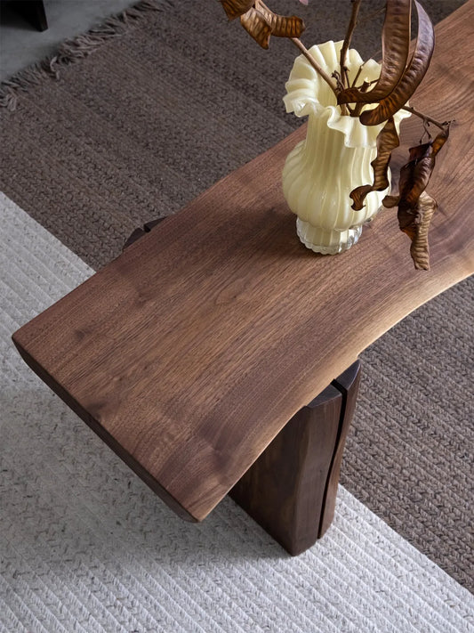 Walnutry Wilder live edge walnut bench front view, showing the balanced slab-leg construction and warm natural finish in a neutral interior.