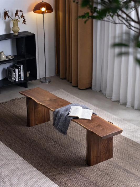 Walnutry Wilder live edge walnut bench placed in a living room setting with layered rugs and soft styling, highlighting its long profile and natural wood character.