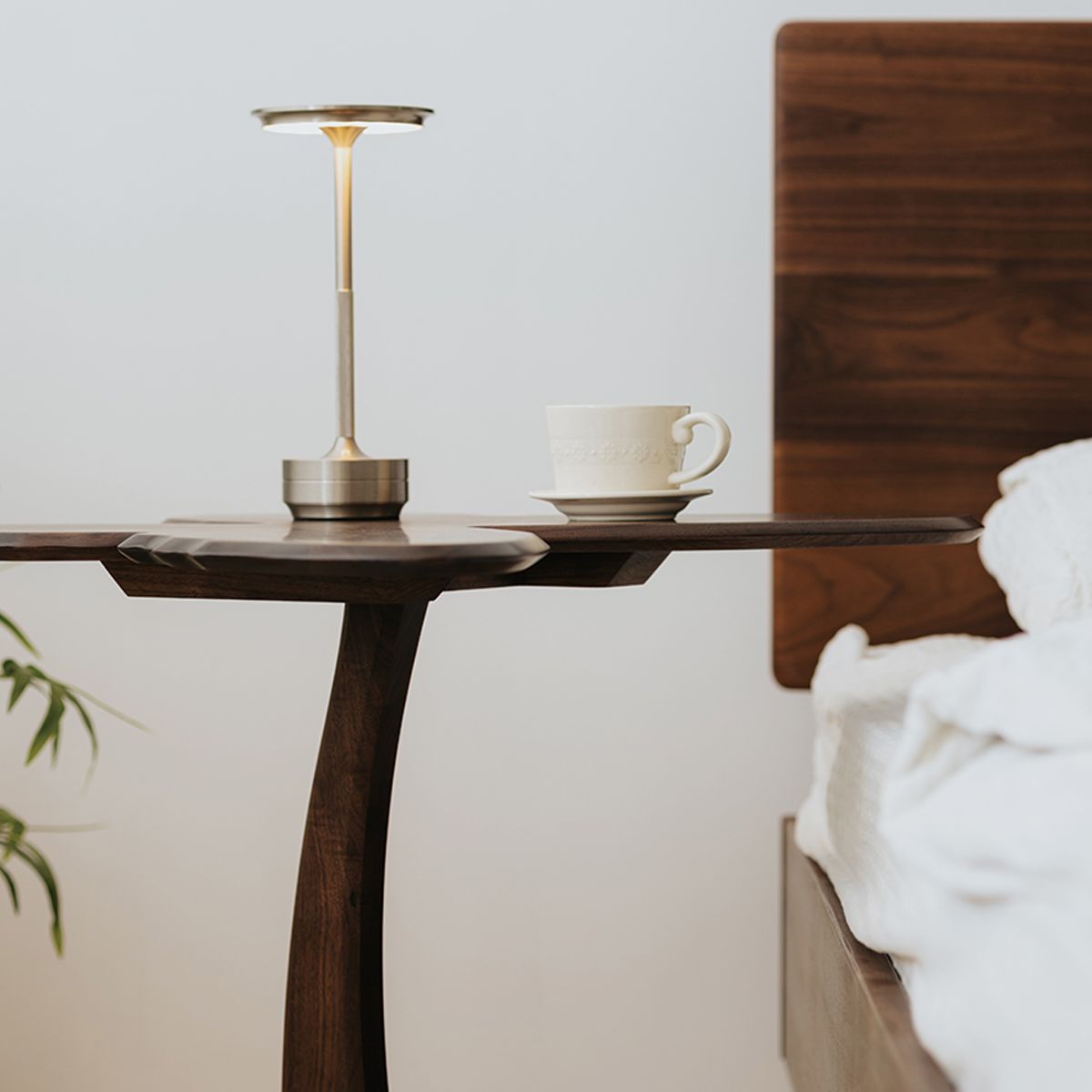 Solid wood whimsical nightstand with modern table lamp and white cup next to wooden bed
