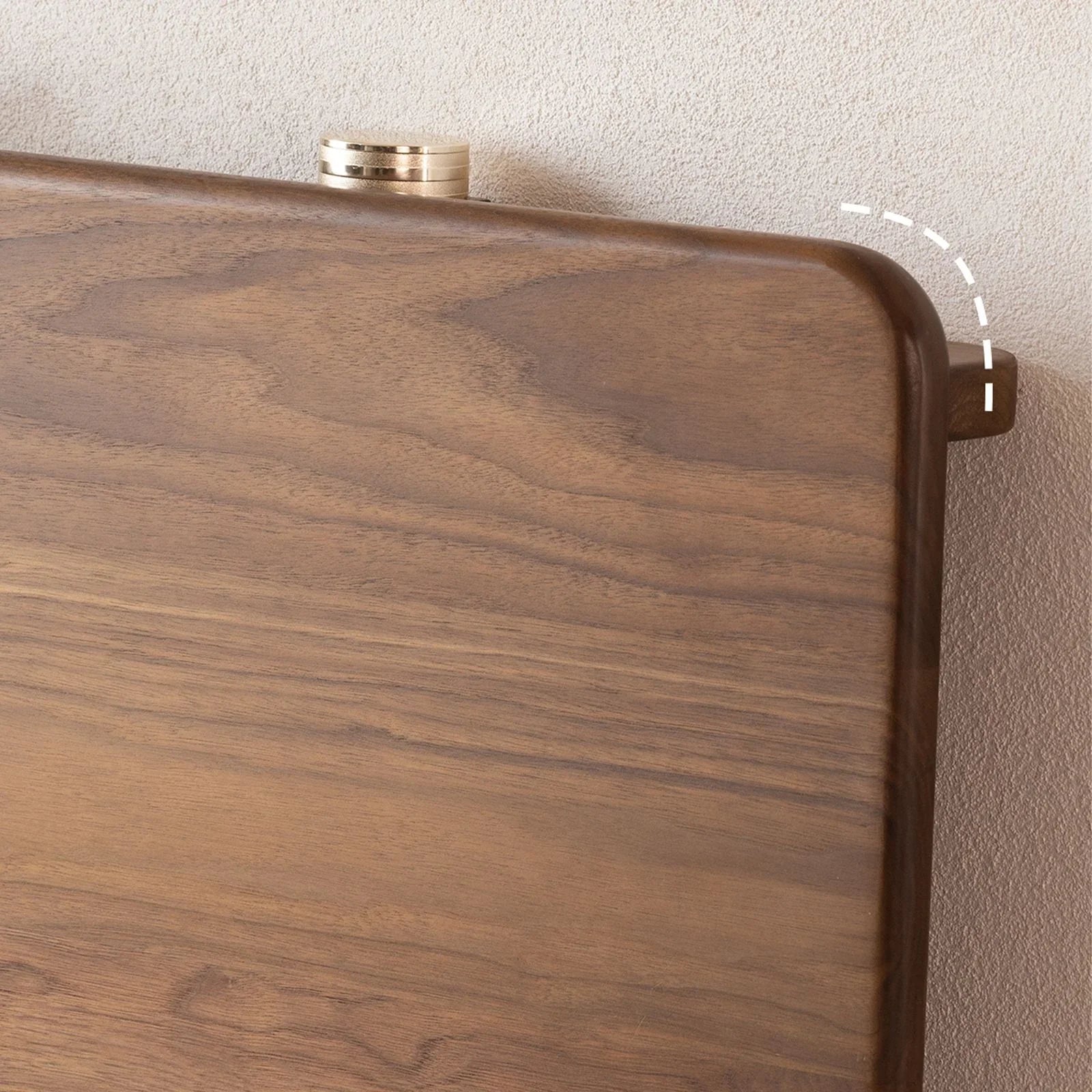 Close-up of smooth walnut wood wide plank headboard with rounded edges against textured wall