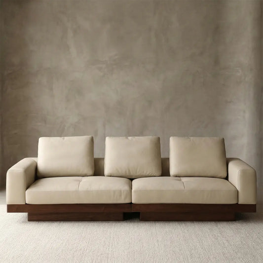 Full view of the extra-wide 110 inch walnut sofa against a concrete wall, styled in a wabi-sabi industrial loft.